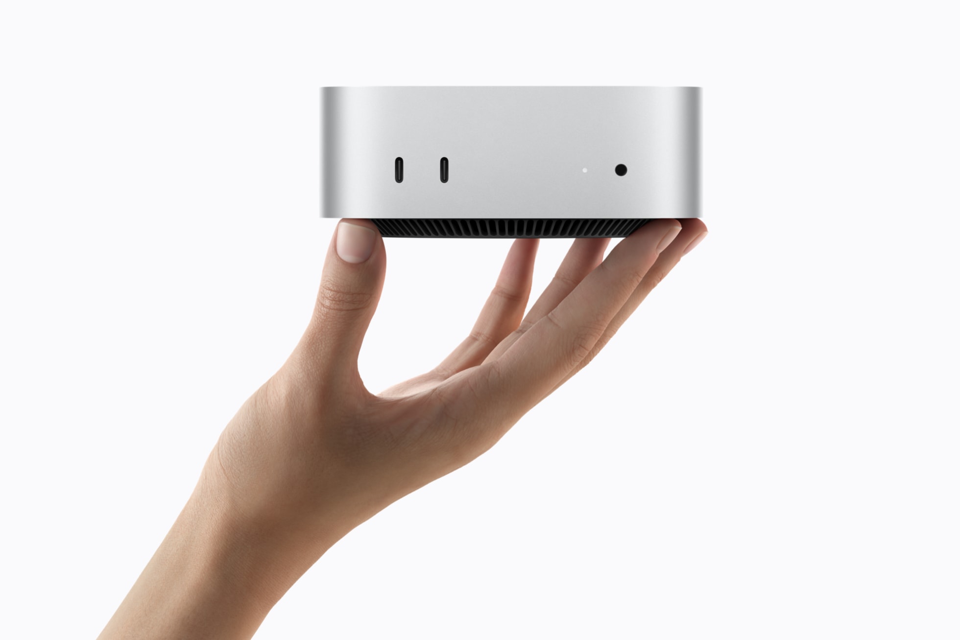 Official Apple product photograph of the 2026 Mac mini, a small square silver aluminium desktop computer with rounded corners and a dark circular base, shown at a three quarter angle against a plain light background.