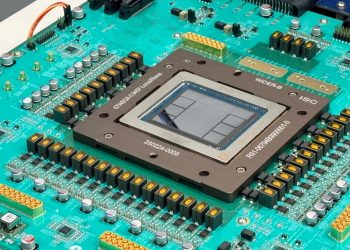 Close-up photograph of the Jalapeño package mounted on a teal green test board, a large square heat spreader frame around an exposed silicon die, surrounded by rows of gold capacitors and connectors, with a Broadcom logo visible at the bottom edge of the board.