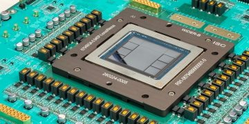 Close-up photograph of the Jalapeño package mounted on a teal green test board, a large square heat spreader frame around an exposed silicon die, surrounded by rows of gold capacitors and connectors, with a Broadcom logo visible at the bottom edge of the board.