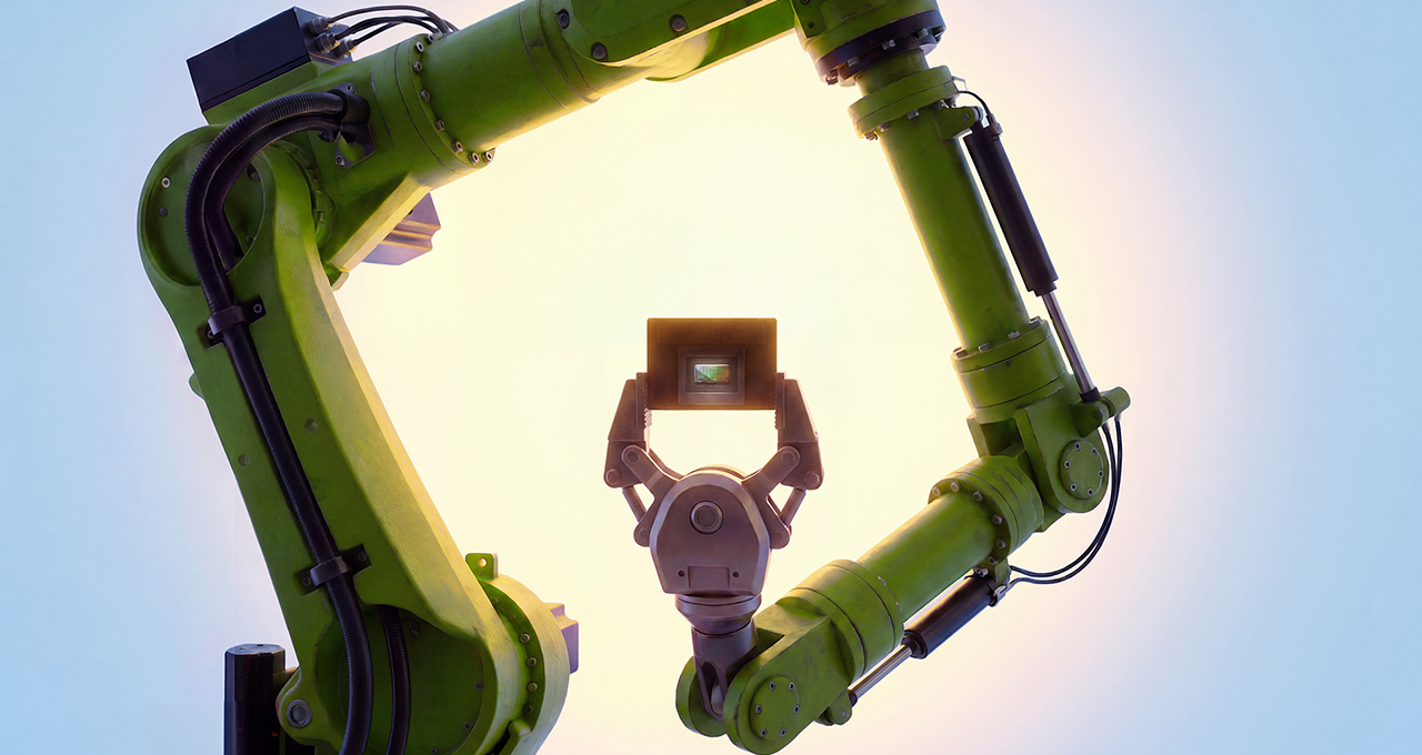 Two green industrial robotic arms reach in from the edges of a bright frame, one gripper holding up a small NVIDIA Jetson module against a soft backlit background.