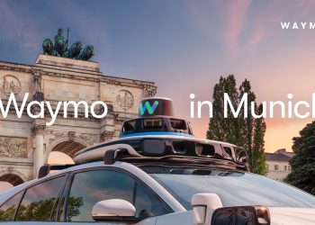 Official Waymo announcement image of a white Jaguar I-PACE with a roof mounted sensor dome parked in front of the Siegestor arch in Munich at sunset, with the caption Waymo in Munich.