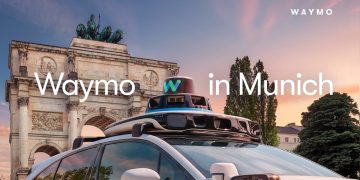 Official Waymo announcement image of a white Jaguar I-PACE with a roof mounted sensor dome parked in front of the Siegestor arch in Munich at sunset, with the caption Waymo in Munich.