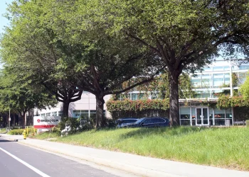 Broadcom Inc. headquarters in San Jose, California: the Broadcom sign by the roadside and an office building with a glass entrance behind a row of trees