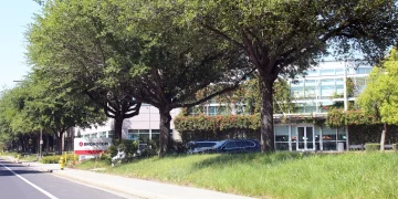 Broadcom Inc. headquarters in San Jose, California: the Broadcom sign by the roadside and an office building with a glass entrance behind a row of trees