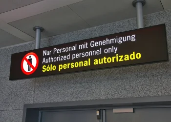 Overhead illuminated sign reading Authorized personnel only in German, English and Spanish, above a closed door