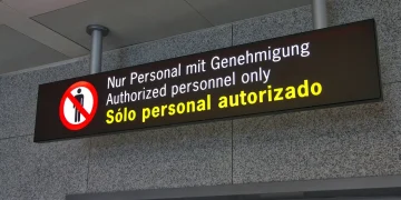 Overhead illuminated sign reading Authorized personnel only in German, English and Spanish, above a closed door