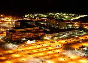 Night aerial photograph of the National Security Agency campus at Fort Meade, Maryland, with glass office blocks and floodlit parking lots
