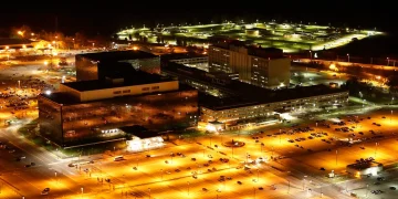 Night aerial photograph of the National Security Agency campus at Fort Meade, Maryland, with glass office blocks and floodlit parking lots
