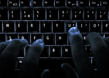 Hands typing on a backlit laptop keyboard in the dark