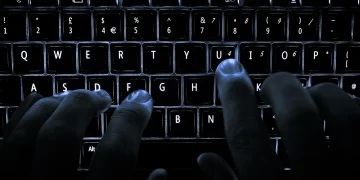 Hands typing on a backlit laptop keyboard in the dark