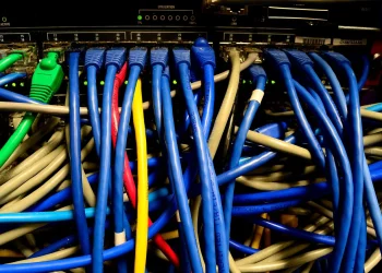 Blue, grey, green, red and yellow Ethernet patch cables plugged into the ports of a rack-mounted network switch
