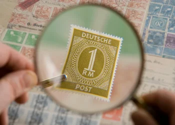 Magnifying glass held over an old postage stamp collection, showing a Deutsche Post 1 Reichsmark stamp enlarged