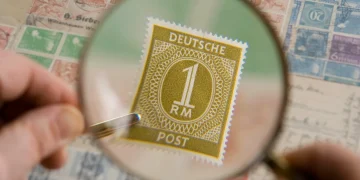 Magnifying glass held over an old postage stamp collection, showing a Deutsche Post 1 Reichsmark stamp enlarged