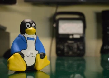 Tux the Linux penguin mascot as a small figurine holding an IBM Software label, on a workbench