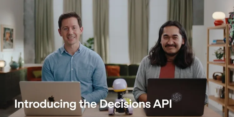 OpenAI's announcement video still for the Decisions API: two presenters at a table with laptops and the caption 'Introducing the Decisions API'