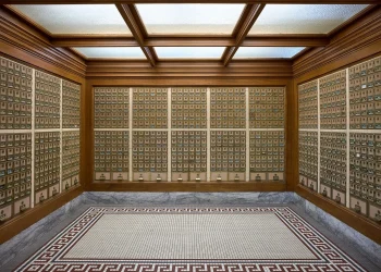 Room lined with rows of brass post office boxes on wood-paneled walls, with a tiled floor and a glazed ceiling