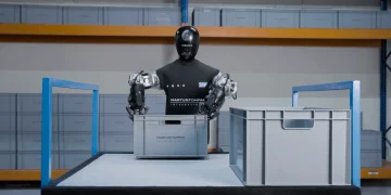 The HMND 01 Alpha humanoid robot with a black head and two gripper arms handling a gray crate in a warehouse during a pilot with SAP and Martur Fompak