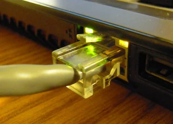 RJ45 Ethernet cable plugged into the network port of a laptop, link LEDs glowing green and amber