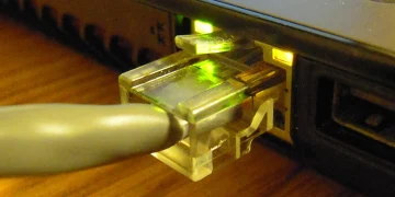 RJ45 Ethernet cable plugged into the network port of a laptop, link LEDs glowing green and amber