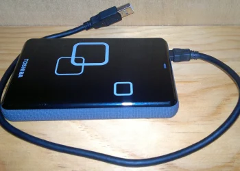 Toshiba 1 TB 2.5 inch external USB hard drive with its USB cable lying on a wooden shelf