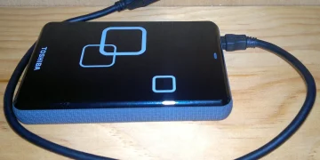 Toshiba 1 TB 2.5 inch external USB hard drive with its USB cable lying on a wooden shelf