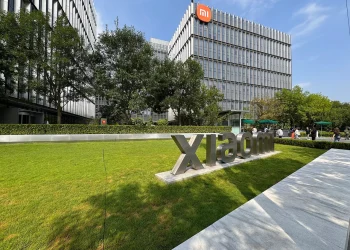 Xiaomi Science and Technology Park in Beijing: large metal Xiaomi lettering on a lawn in front of glass office buildings, one carrying the orange Mi logo