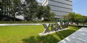 Xiaomi Science and Technology Park in Beijing: large metal Xiaomi lettering on a lawn in front of glass office buildings, one carrying the orange Mi logo