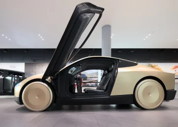 A gold Tesla Cybercab concept robotaxi with its door raised, seen from the side in a Tesla showroom