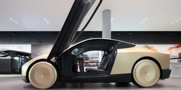 A gold Tesla Cybercab concept robotaxi with its door raised, seen from the side in a Tesla showroom