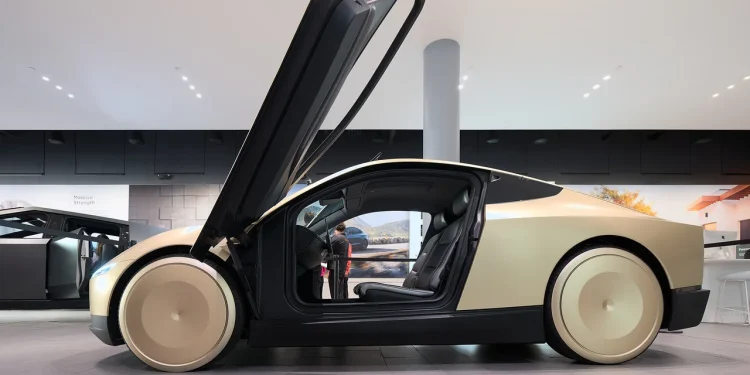 A gold Tesla Cybercab concept robotaxi with its door raised, seen from the side in a Tesla showroom