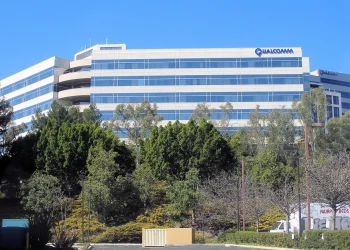 Qualcomm headquarters office building in San Diego with the company name on its roofline, seen behind trees under a blue sky