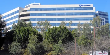 Qualcomm headquarters office building in San Diego with the company name on its roofline, seen behind trees under a blue sky