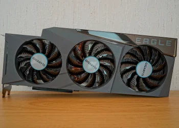 Gigabyte GeForce RTX 3090 Eagle OC 24G graphics card with three fans standing on a wooden table in front of a textured white wall