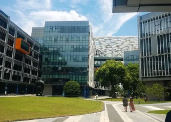Courtyard of the Alibaba Group Binjiang campus in Hangzhou, with glass and steel office buildings, a white lattice-patterned bridge structure and a lawn under a blue sky