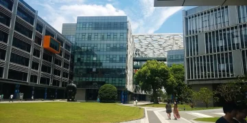 Courtyard of the Alibaba Group Binjiang campus in Hangzhou, with glass and steel office buildings, a white lattice-patterned bridge structure and a lawn under a blue sky