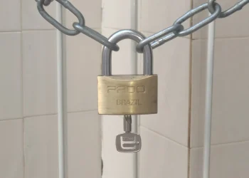 Brass padlock with its key still in the lock, closed on a steel chain in front of a tiled wall