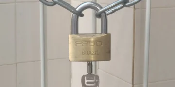 Brass padlock with its key still in the lock, closed on a steel chain in front of a tiled wall