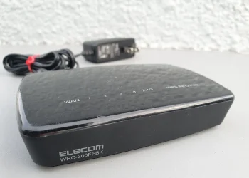 ELECOM WRC-300FEBK Wi-Fi router with WAN and LAN port labels on top, lying next to its power adapter