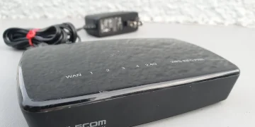ELECOM WRC-300FEBK Wi-Fi router with WAN and LAN port labels on top, lying next to its power adapter
