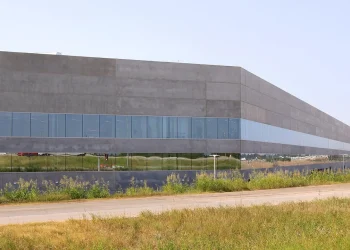 Exterior of Tesla Gigafactory Texas Building 1 near Austin, a long concrete and glass factory wall beside a road