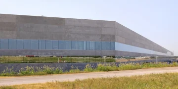 Exterior of Tesla Gigafactory Texas Building 1 near Austin, a long concrete and glass factory wall beside a road