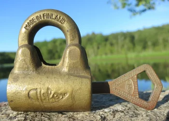 Mid 20th century brass padlock with its key lying next to it on a rock, lake and forest in the background