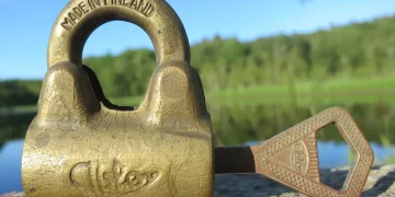 Mid 20th century brass padlock with its key lying next to it on a rock, lake and forest in the background